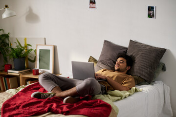 Young man lying on bed in the bedroom and using laptop for watching movie