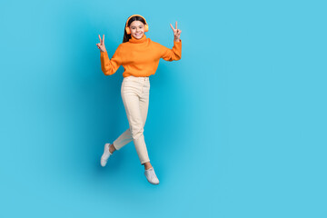 Full body portrait of cute energetic girl jumping show v-sign empty space isolated on blue color background