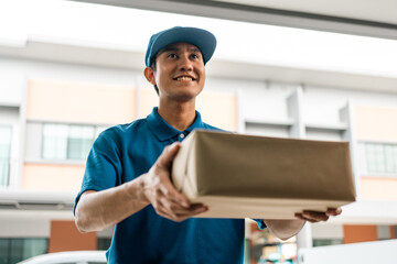 Asian delivery man with parcel in hand of blue uniform sending parcel to customer front of the house from shopping online with good service. Courier man send a package to destination.