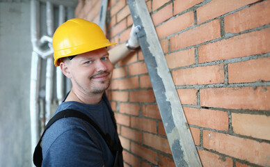 Male builder mason makes brickwork of walls and holds working tool. Construction services concept