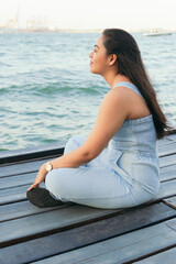 Fototapeta na wymiar Young Woman pensive while sitting on a lake dock during a beautiful summer day.