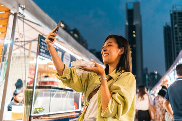 Naklejka premium Asian woman enjoy eating fries street food at night market. Traveler Asian blogger women Happy tourists Beautiful female with Traditional thailand bangkok food.