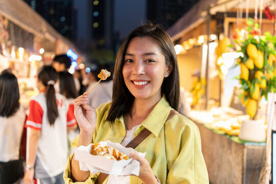 Asian woman enjoy eating fries street food at night market. Traveler Asian blogger women Happy tourists Beautiful female with Traditional thailand bangkok food.
