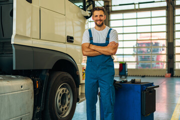 Portrait of professional truck mechanic standing in vehicle workshop. In background parked trucks...