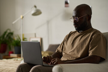 African American man concentrating on his online work on laptop while sitting on armchair in the room