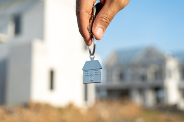 Close up male hand holding house key with sunlight. Real estate agent at construction site. New home purchase sales or rent. Choose Planning to buy property
