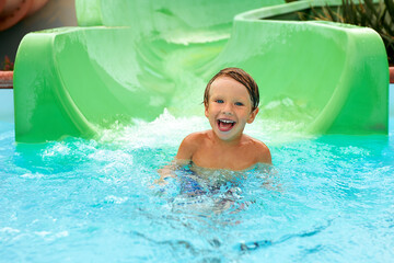 Joyful boy descends from the water slide in the water park, children's attractions in the water...