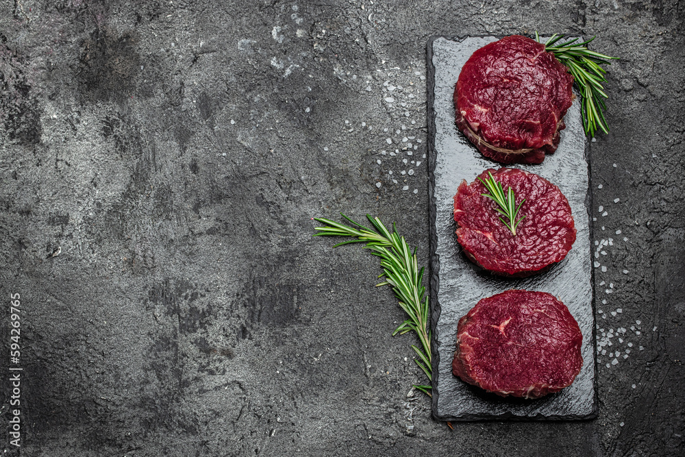 Wall mural beef meat on a dark background, whole piece of tenderloin with steaks and spices ready to cook