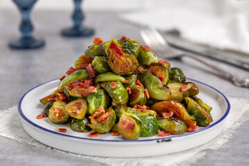Sauteed Brussels Sprouts with Bacon. Caramelized Brussels sprout halves with bacon served on white ceramic plate. Selective focus, horizontal, light grey concrete background.