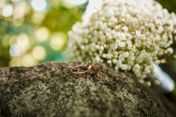Two golden wedding rings on a stone, a bouquet of white flowers of the bride in the background