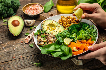 Girl holding plate with hands vegan breakfast. meal in bowl with avocado, mushrooms, broccoli, spinach, chickpeas, pumpkin. top view