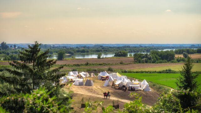 Two noblemen, hussars, riding on horses to tent encampment. Slavic or Viking tent camp on a field, next to Vistula River and Gniew city, Poland