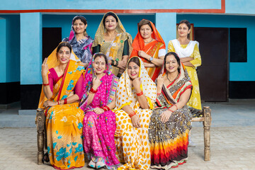 Group of happy young traditional indian women housewives wearing colorful sari sitting looking at...