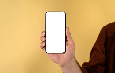 Fototapeta na wymiar Cropped hand of male entrepreneur showing smart phone with blank white screen for brand promotion. Young man holding cellphone with empty free space for advertisement on beige background