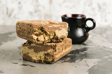 Appetizing pieces of halva with cocoa and coffee in a cup on a light gray concrete background