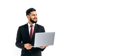 Copy-space. Panoramic photo of positive handsome elegant indian or arabian man in business suit, executive, holding an open laptop in hands, looking aside, stand on isolated white background, smiles