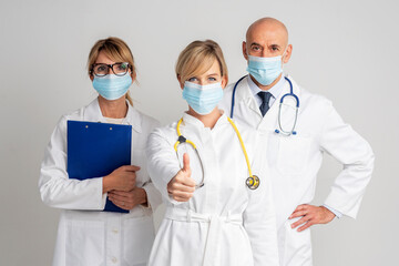Group of medical people wearing face mask and showing thumb-up at isolated white background