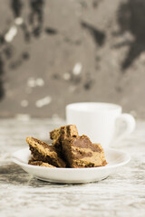 Delicious halva with cocoa on a white plate and a cup of espresso on a light gray concrete background
