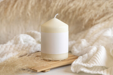 Candle with label on wooden tray near pampas grass and cosy sweater, Close up, mock up