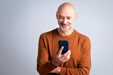 Portrait of a confident mature man with bald head using cellphone and text messaging against isolated background
