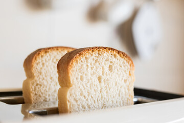 Close-up white slices of sliced bread sticking out in a white toaster, selective soft focus. - obrazy, fototapety, plakaty