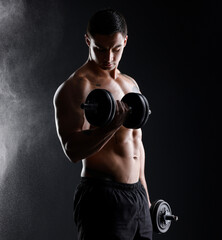Fototapeta na wymiar Lift and live life with no regrets. an athletic man lifting dumbbells against a dark background.