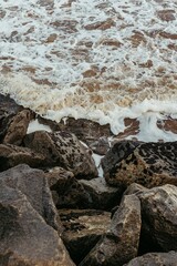 Vertical shot of waves crashing on the massive rocks on the beach, perfect for wallpapers