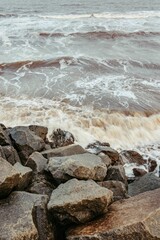 Fototapeta premium Vertical shot of waves crashing on the massive rocks on the beach, perfect for wallpapers