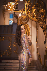 Portrait of a gorgeous young brunette girl in a shiny ivory-sequined dress with an open back...