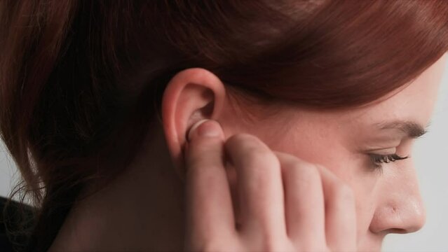 modern technology, young woman inserts wireless headphones into her ear to listen to music, close-up