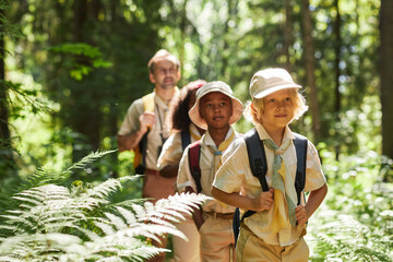 Waist up portrait of cute boy with group of scouts hiking in forest lit by sunlight, copy space
