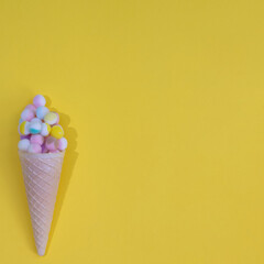 Fluffy balls of various colors in an ice cream cone, with copy space, on a yellow background. Minimal flat lay scenes.