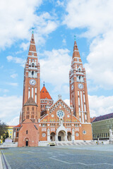 A grand, historic votive church in Szeged Hungary with its imposing tower and beautiful brick facade stands proudly amongst the bustling cityscape.