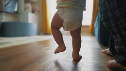 baby takes the first steps to learn. happy family kid dream concept. mom teaches baby newborn to walk and take first steps. mom light holding baby hands teaches to walk silhouette from window - Powered by Adobe