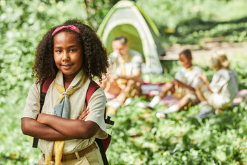 Waist up portrait of cute black girl scout looking at camera while camping with school group, copy space