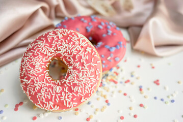 Two fresh sweet glazed donuts on the table, the background is decorated with draped fabric and bokeh