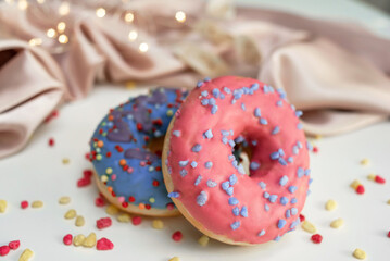 Two fresh sweet glazed donuts on the table, the background is decorated with draped fabric and bokeh