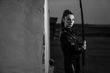 Grayscale of female in black ninja assassin costume holding a sword and standing near wall