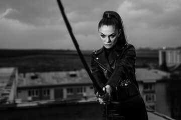 Grayscale of female in black ninja assassin costume holding a sword and standing near wall