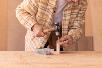 Crop anonymous carpenter hammering nail into wooden blocks at workbench while working in home...