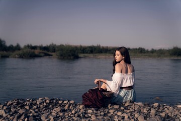 Female with a white dress sitting on the beach, a basket with clothes near