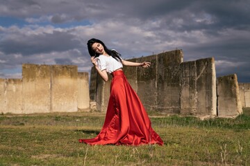 Young beautiful female in a white shirt and red skirt posing near ancient ruins