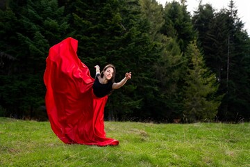 Young beautiful dancer female in a flowing red dress posing in a park