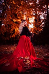 Beautiful young female in a red dress posing in a vibrant autumn forest