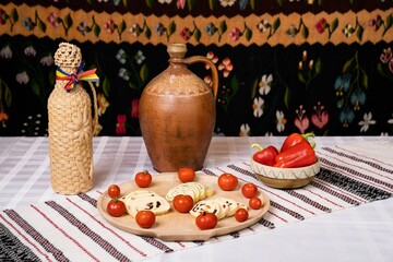 Rustic table with a jug, wicker-wrapped bottle, cheese roll-ups, cherry tomatoes, and red peppers.