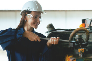 A happy young woman worker of a large machinery maintenance factory in a blue dress and a white...