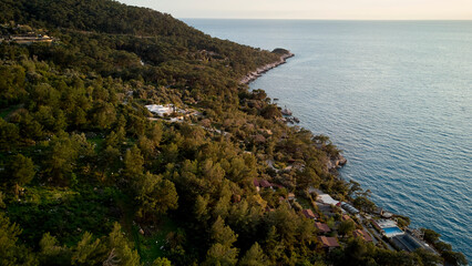 A breathtaking view of Turkeys Faralya Coast, featuring a tranquil shoreline dotted with trees and cliffs against an expansive horizon over the sea.