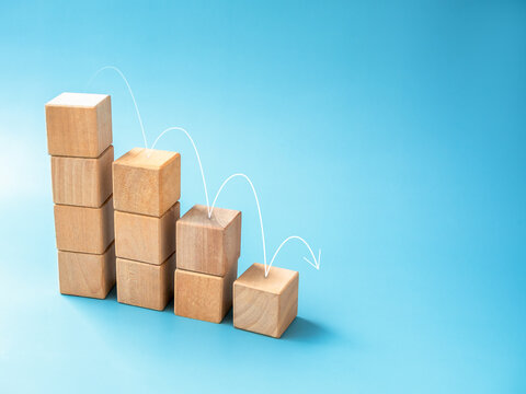 The arrow bounces down from the top point on wooden block stack as a graph step on blue background with copy space. Inflation, economic collapse, decrease money and business financial crisis concepts.