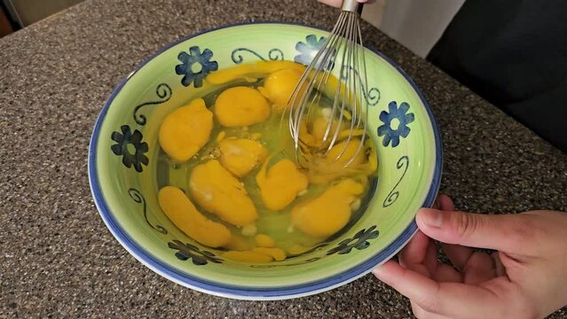Breaking up egg yolks in food preparation bowl with wire whisk