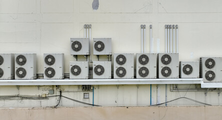 Many condensing units of air conditioners are installed on concrete building wall. Air conditioner...